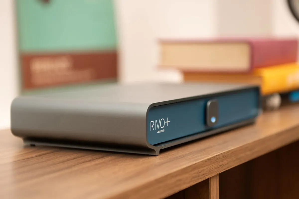 Rivo+ in the Classic finish on a wooden shelf, in front of a stack of books.